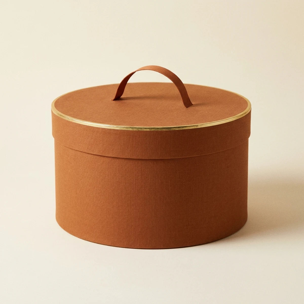 Cognacfarvet rund hatteæske med guldkant og bærehåndtag